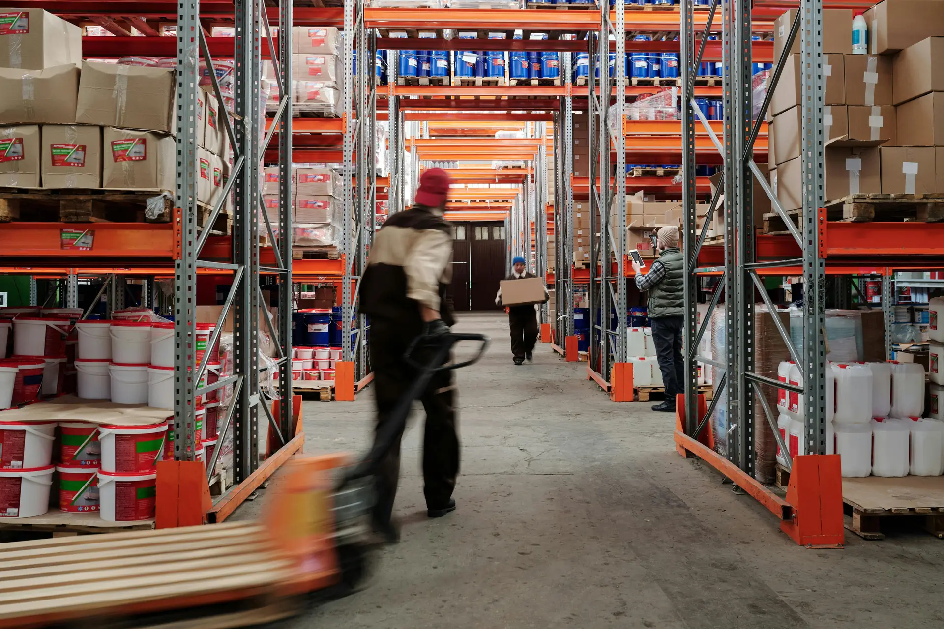 Worker moving a pallet truck down a racking aisle in a distribution warehouse