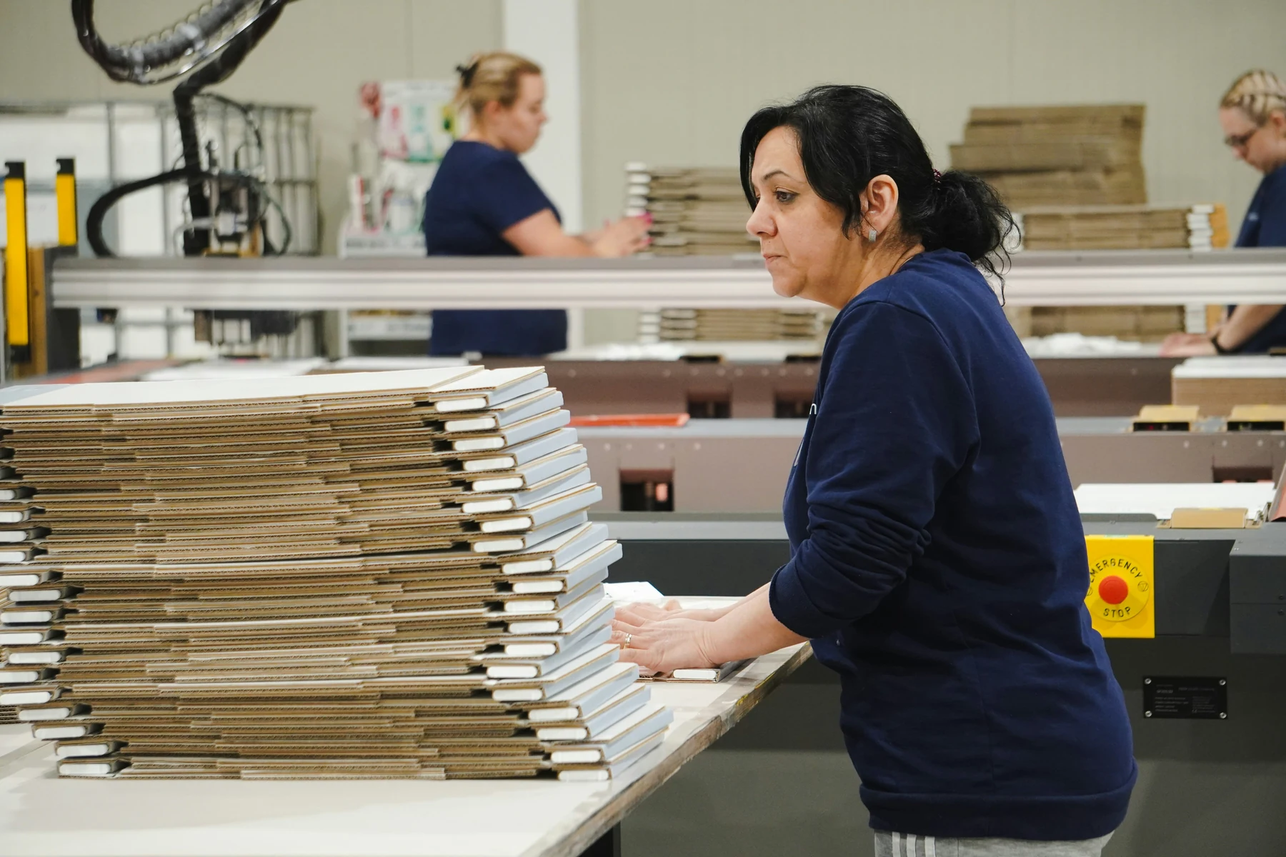 Operators working a carton converting line, finished blanks stacked alongside